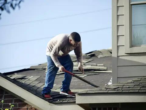 Roofer removing old shingles during a tear-off
